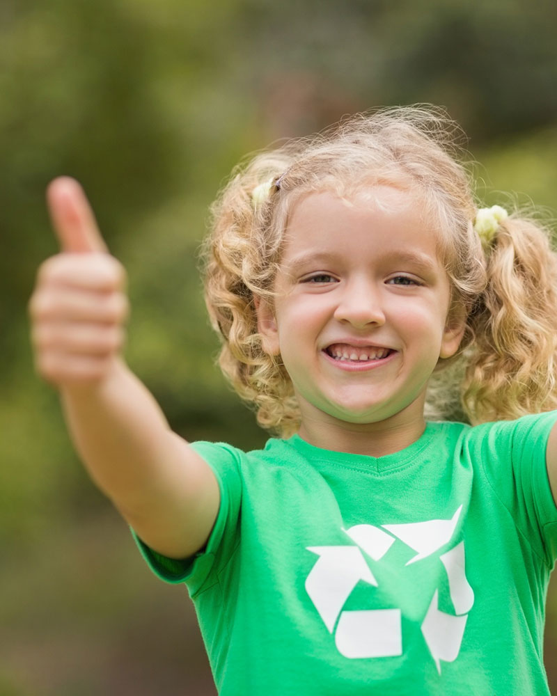 A young girl holding up thumbs up, wearing a green t-shirt with recycling logo on it.